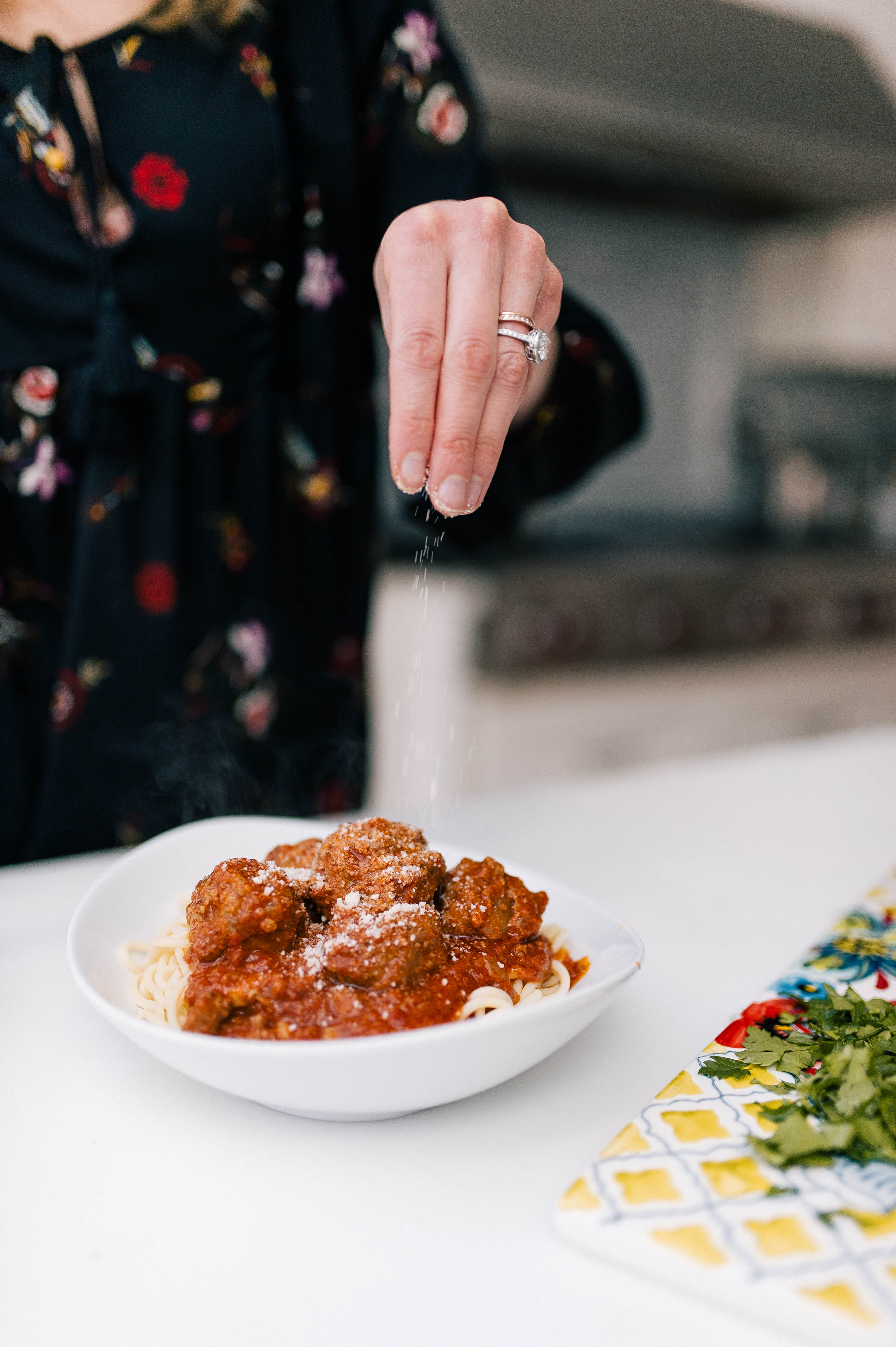 Eva Amurri sprinkles parmesan cheese on top of a bowl of spaghetti and slow cooker meatballs