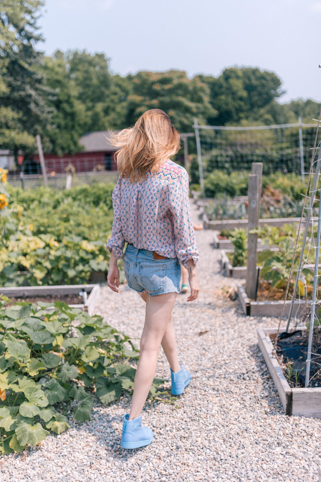 Eva Amurri Martino wears a silk blouse and denim cutoffs and walks through the vegetable garden of a local farm