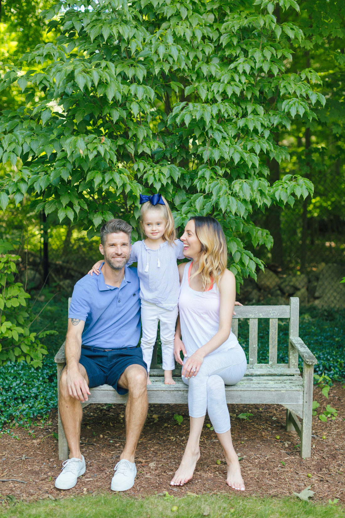 Eva Amurri Martino and Kyle Martino sit with four year old daughter marlowe on a bench surrounded by greenery in the yard of their Connecticut home