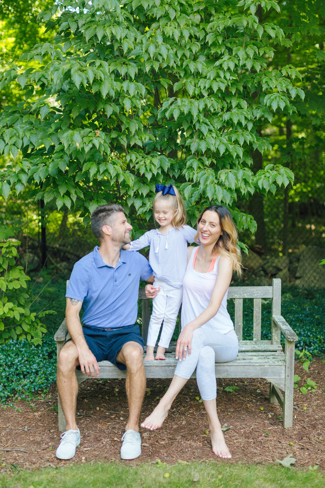 Eva Amurri Martino and Kyle Martino sit with four year old daughter marlowe on a bench surrounded by greenery in the yard of their Connecticut home