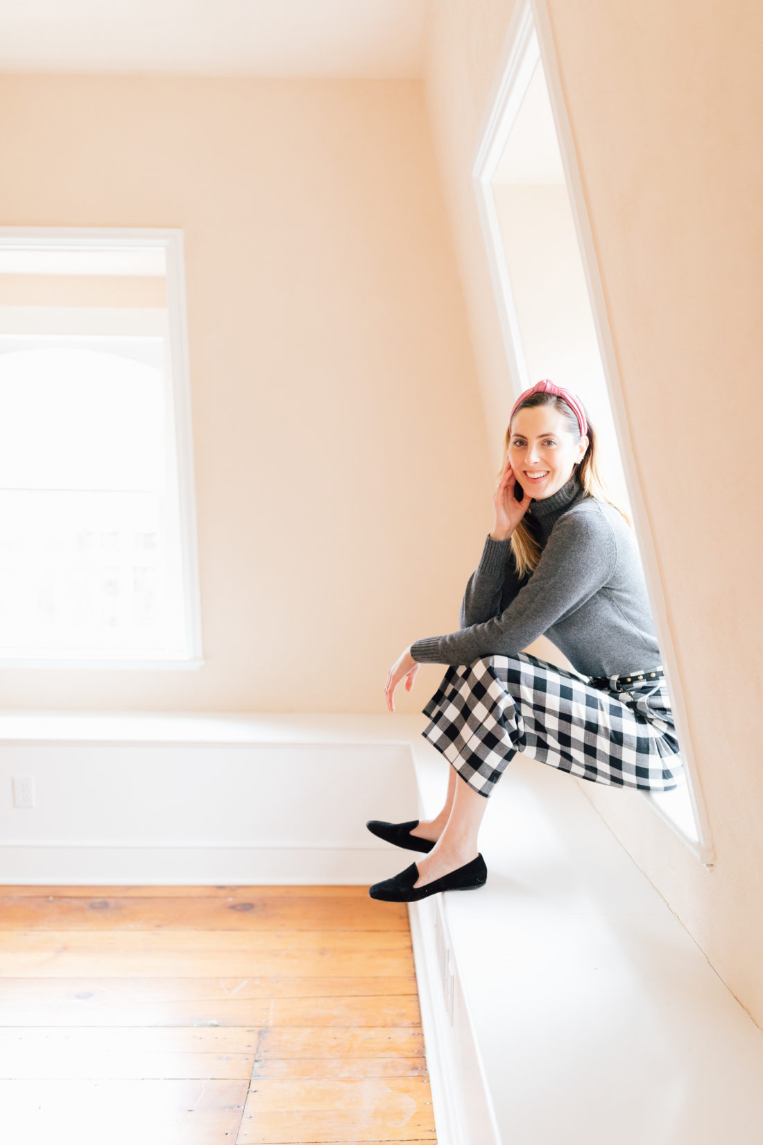Eva Amurri Martino wears checked trousers and a grey cashmere sweater, and sits in her empty home that awaits renovations