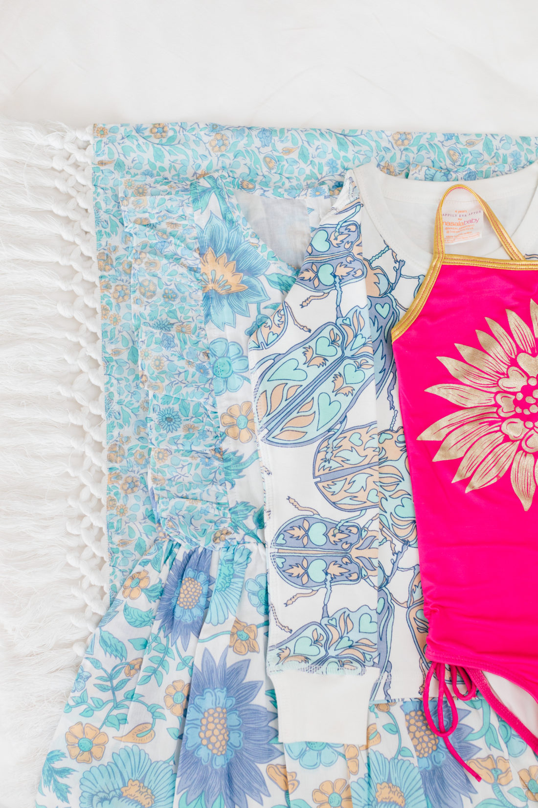 The Happily Eva After x Masala Baby resort capsule collection is layed out on a white background with an array of patterns in blue tones and a pop of color in the bright fuschia bathing suit