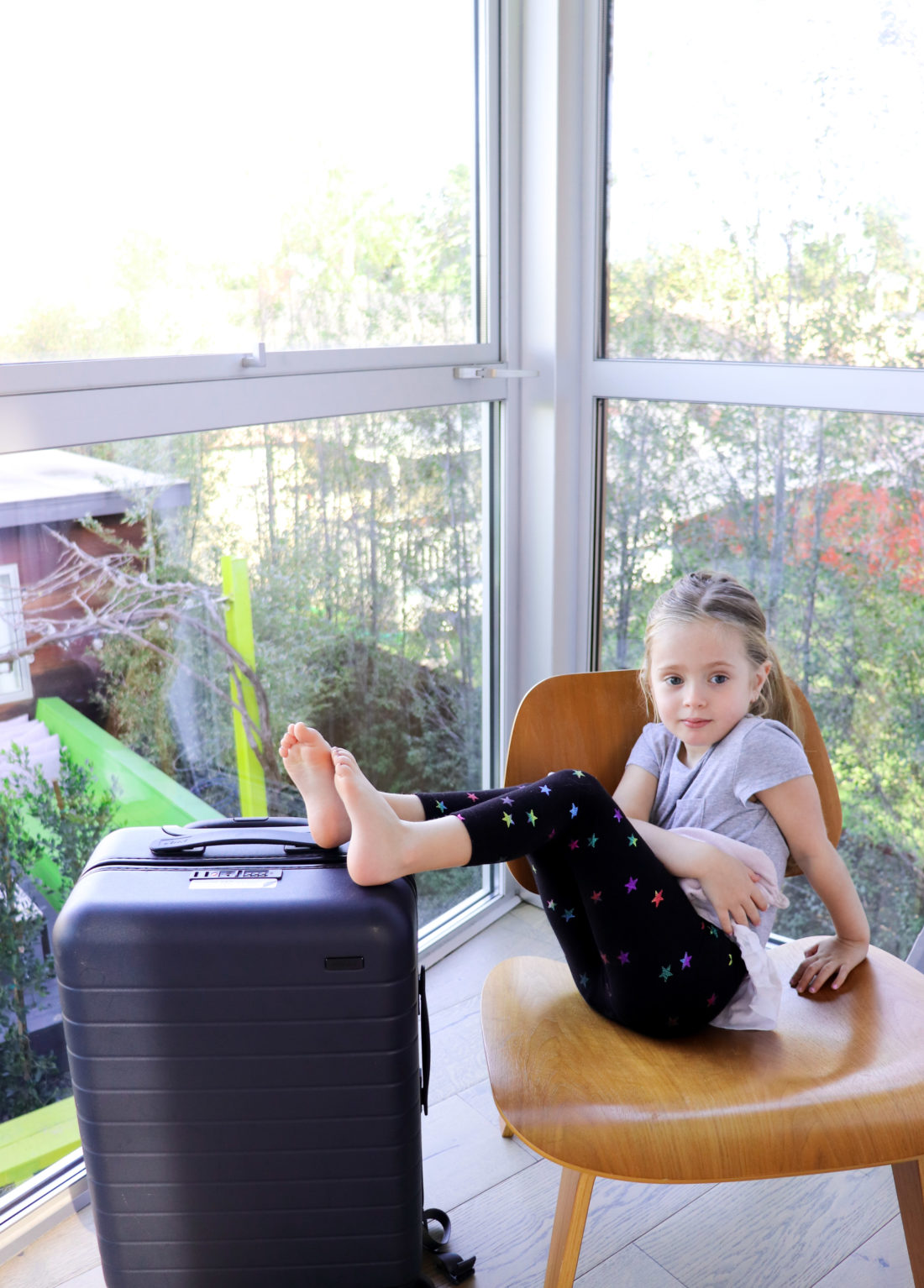 Marlowe Martino sits on a chair and rests her feet on a carry-on suitcase as part of a blog post about the best toddler travel tips