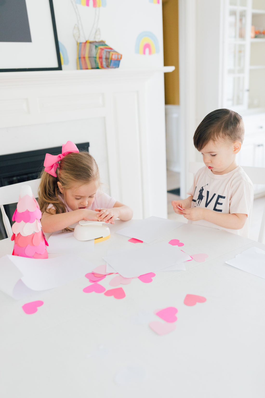 Marlowe and Major martino wear shades of pink and use a large heart hole punch to make materials for a Valentine's Day craft