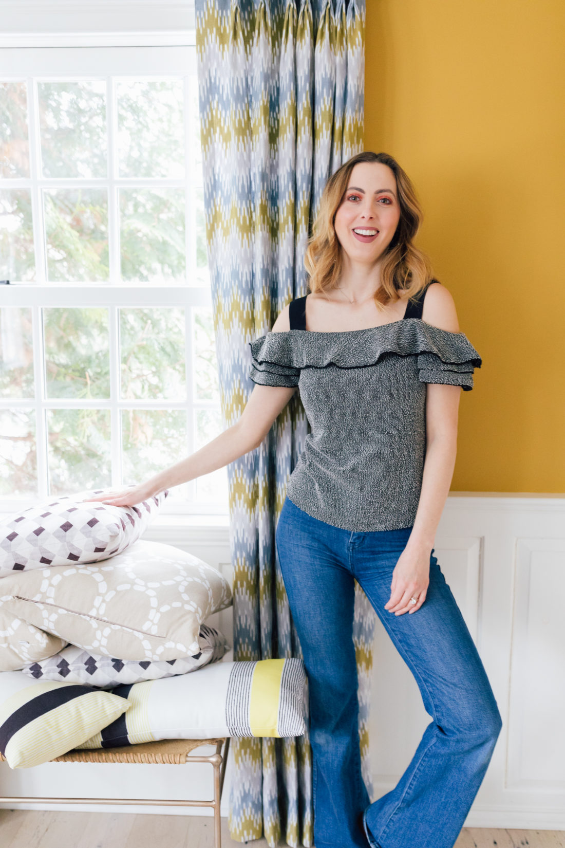 Eva Amurri Martino wears jeans and an off the shoulder top, and stands in the living room of her connecticut home as she prepares to move house