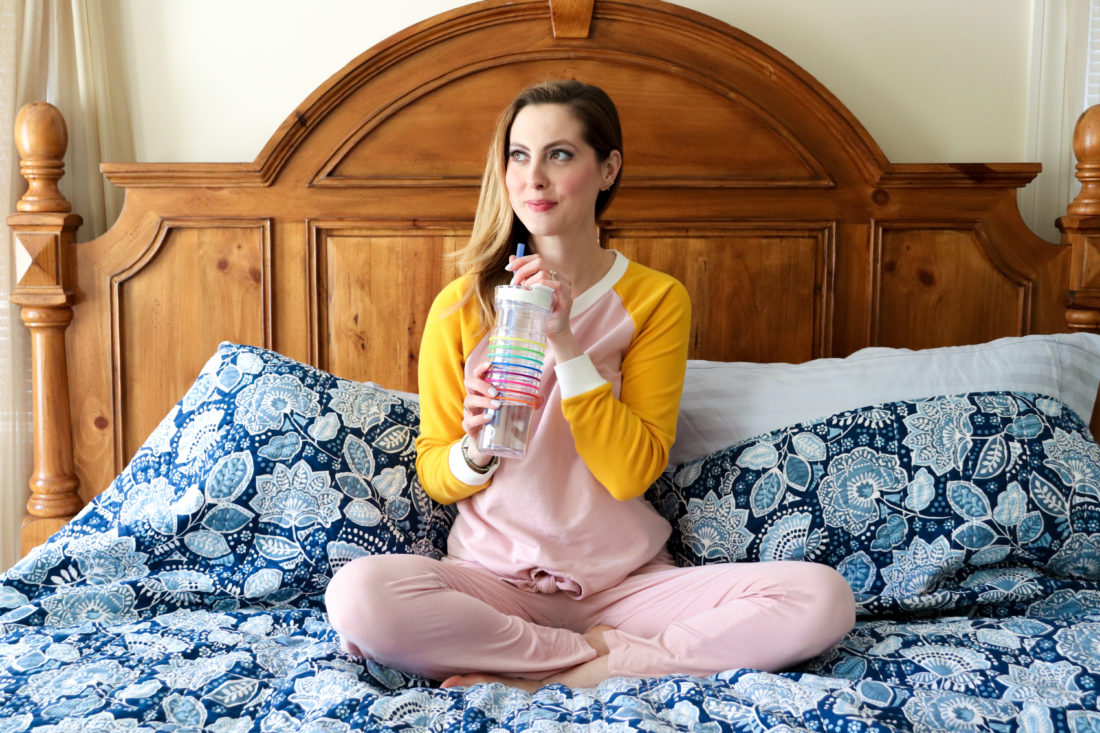 Eva Amurri Martino of Happily Eva After sits on her bed in loungewear drinking water