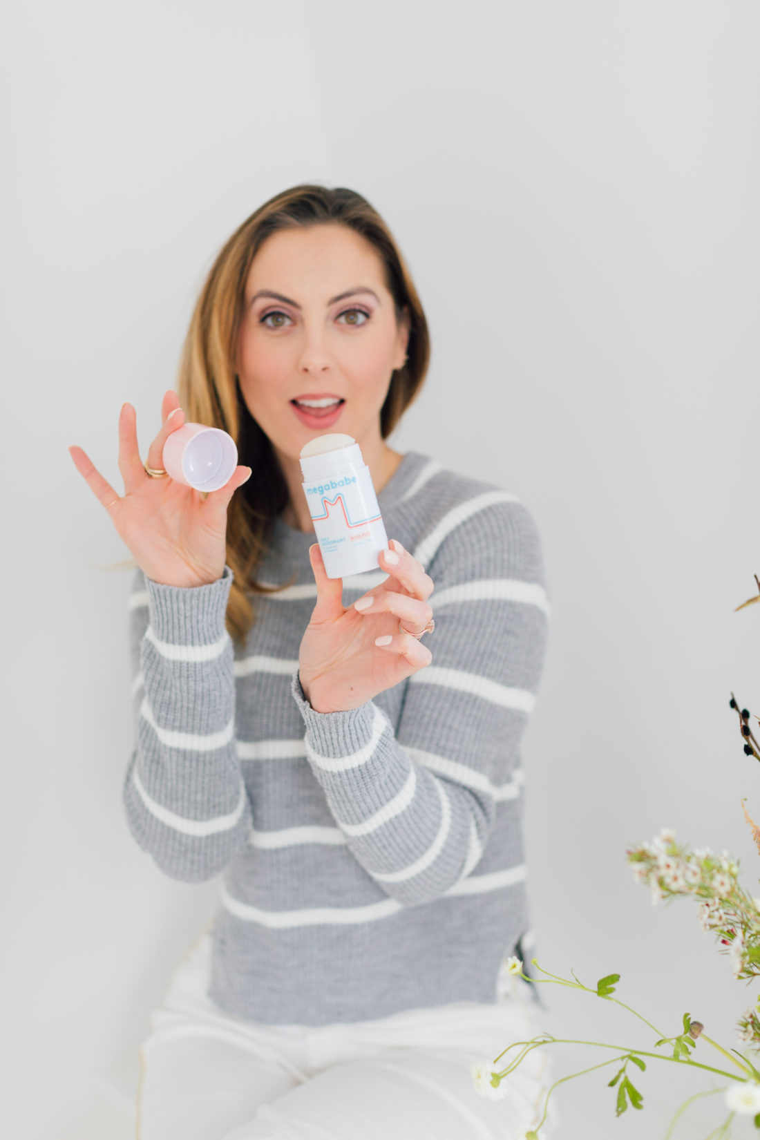 Eva Amurri Martino wears a grey and white striped sweater, and removes the cap on a tube of Megababe deodorant