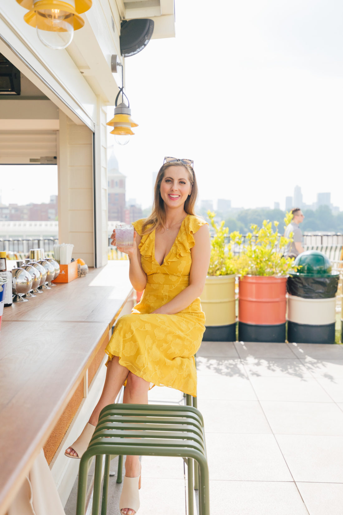 Eva Amurri Martino wears a bright yellow sress and sips on a cocktail at an outdoor bar